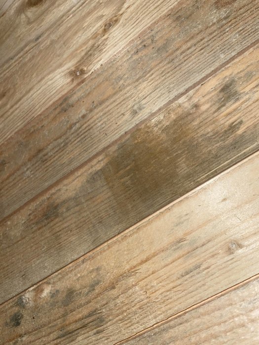 Träplankor på vinden med möjliga mögel- eller fuktfläckar.