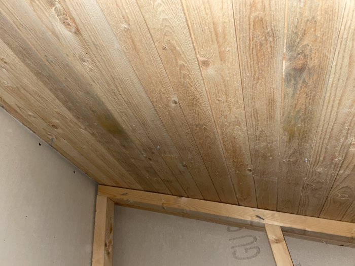 Träpanel på snedtak i en vind eller oinredd del av ett hus, med viss missfärgning.