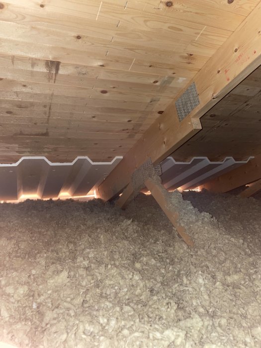 Mörka fläckar på träbjälklag under takisolering i vindutrymme.