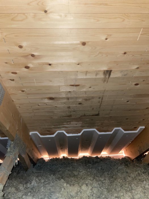 Träbjälklag med mörka fläckar och isolering synlig, möjlig vattenskada eller mögel.