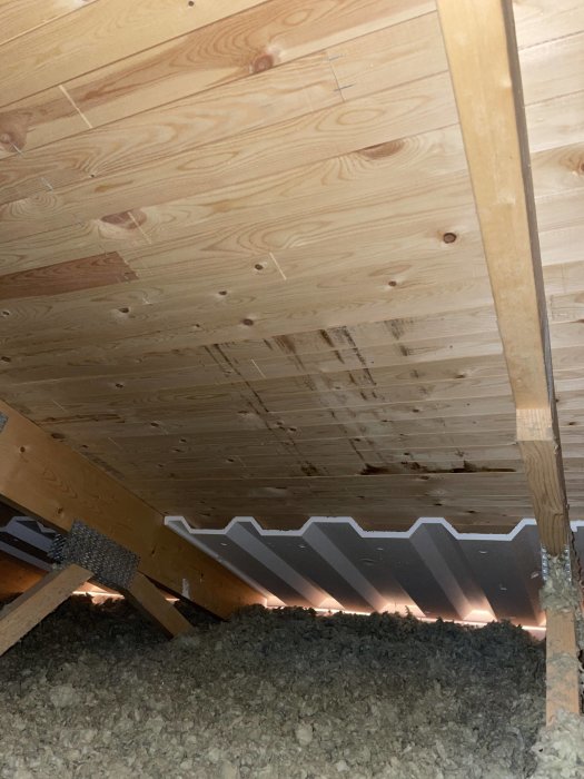 Tak med träpanel och fläckar som syns, samt isolering synlig under takstolarna på vinden.