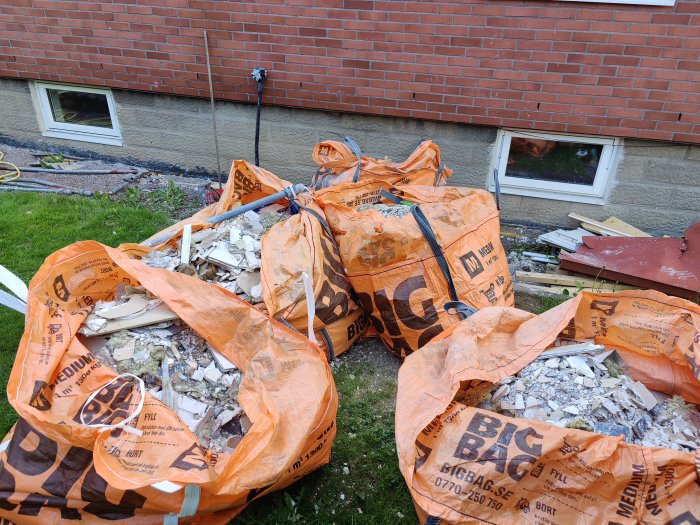 Fem orangea Big Bag-säckar fyllda med fyllnadsmassor framför en röd tegelvägg, redo för upphämtning.