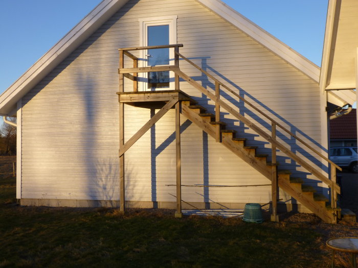 Hus med vit fasad och trätrappa, inklusive hussvalbo under taknocken.