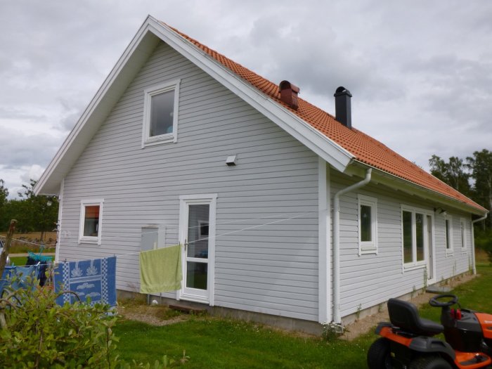 Hus isolerat med cellplast, ljusgrå väggar, röda takpannor, gräsklippare framför huset.