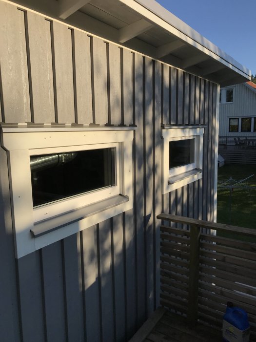 Attefallshus med falsad bandplåt på fasaden och vitmålade fönsterkarmar i soligt väder.