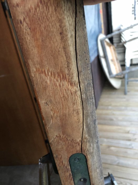 Spricka i en teakdörr vid låskistan som löper uppåt mot dörrkanten, i behov av reparation.