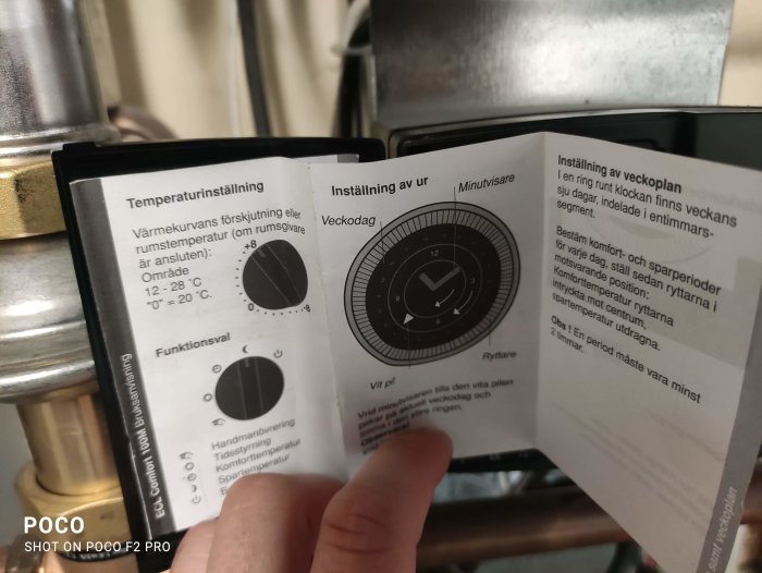 Hand håller manual med instruktioner för temperaturinställning och veckoplan av uppvärmningssystem.