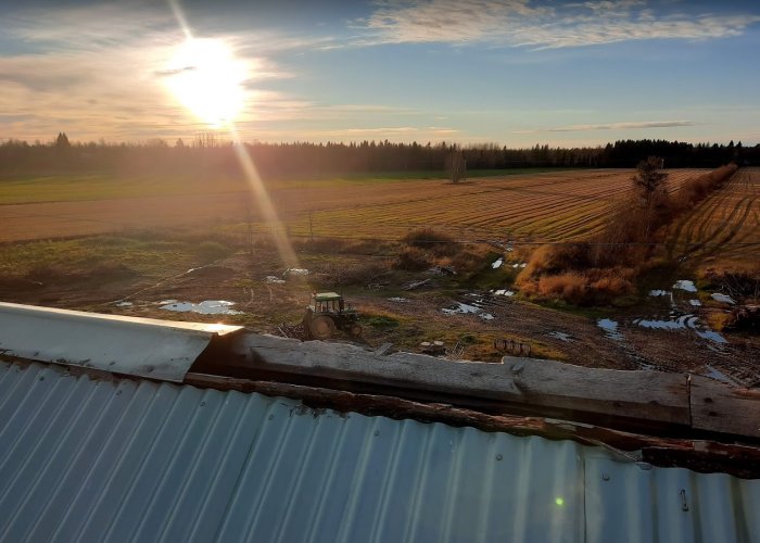 Utsikt från ett tak med solnedgång över ett fält och en traktor, möjlig plats för fallskyddslina.