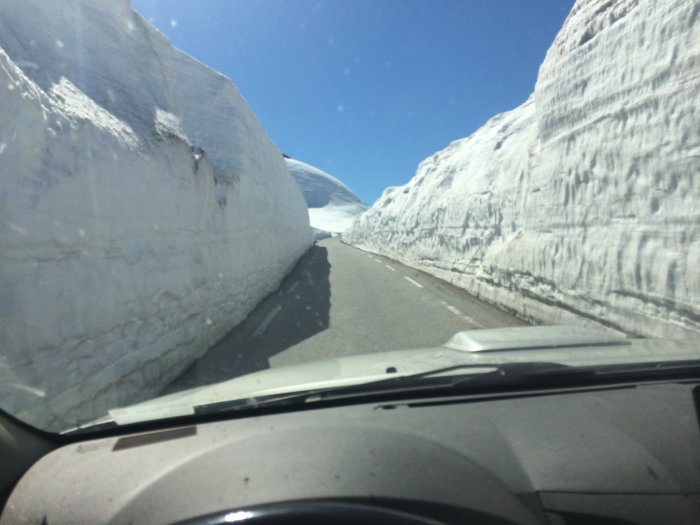 Bil som kör genom en snöig vägklyfta med höga snöväggar under våren.