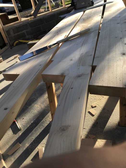 Utsågade träbalkar i dimension 220x45 mm på en byggarbetsplats med såg och tumstock.