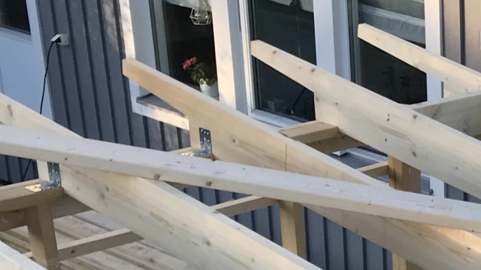 Takstolar under konstruktion, utskurna träbalkar framför husfasad.