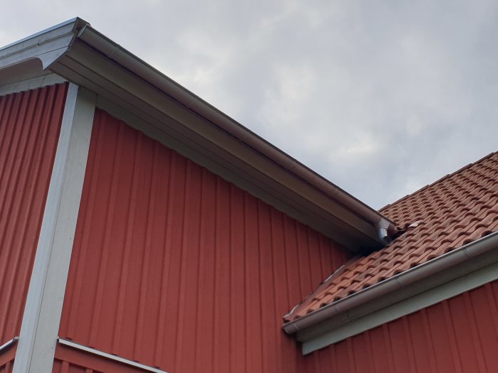 Röd träfasad på ett hus med vitt hörnbeslag och en del av ett tegeltak med takavvattning.