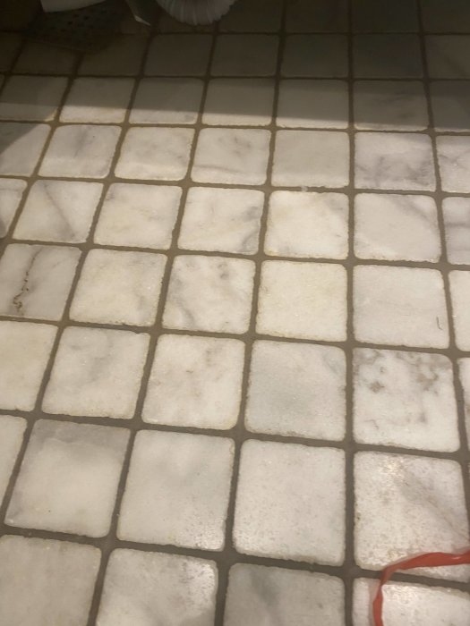 Gammal smutsig kakelgolv med möjlig mögelväxt och missfärgningar under badkaret.