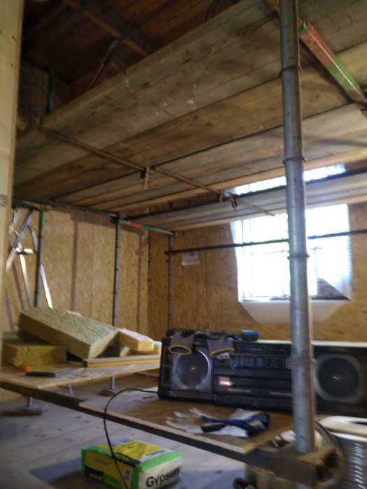 Renoveringsarbete i rum med uppställd ställning, isoleringsmaterial och ett halvfärdigt tak.