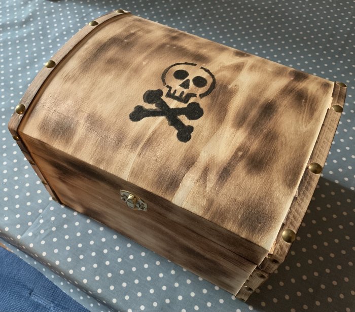 Liten kista med patinerad yta och ett svart skalle-och-korsben på locket.