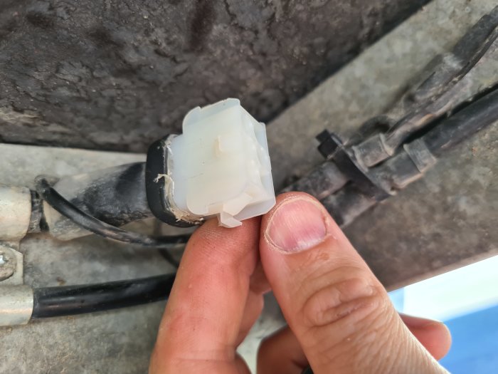 Hand som håller en vit plastkontakt för släpvagnsbelysning nära ett svart kabelskydd.