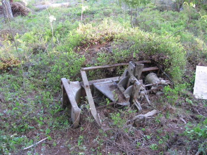 Gamla verktygsdelar i skogen, inklusive en modifierad kedjestämmaskin och handdriven maskindel.