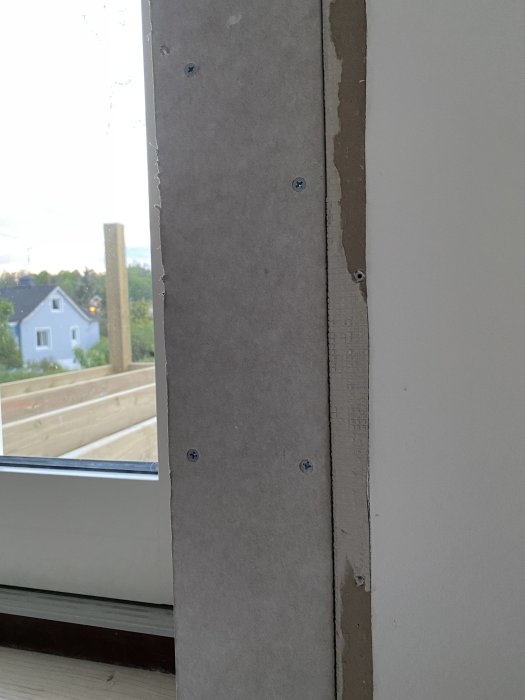 Delvis monterad gipsskiva med synliga skruvar på en vägg nära ett fönster under en renovering.