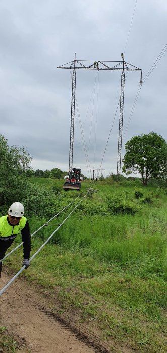 Arbetare i säkerhetshjälm vid installation av kraftledningsstolpar i grönt fält.