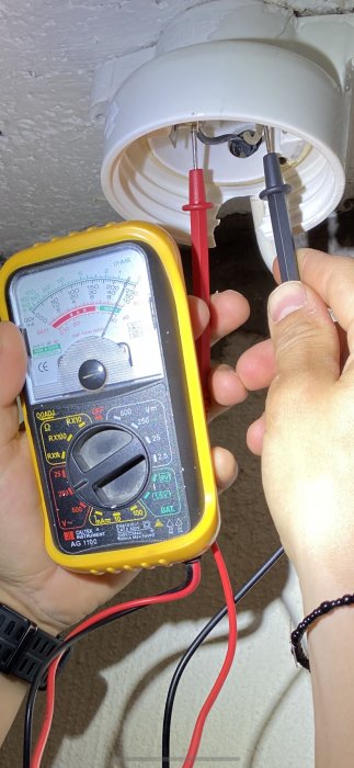 Användare mäter spänningen med multimeter på eluttag för att identifiera fas och tändtråd.