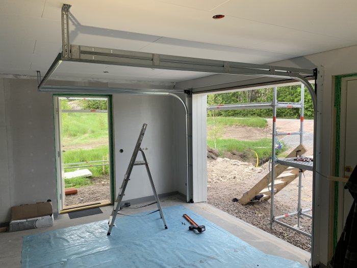 Nyinstallerad garageport i ett garage under renovering med verktyg och stege.