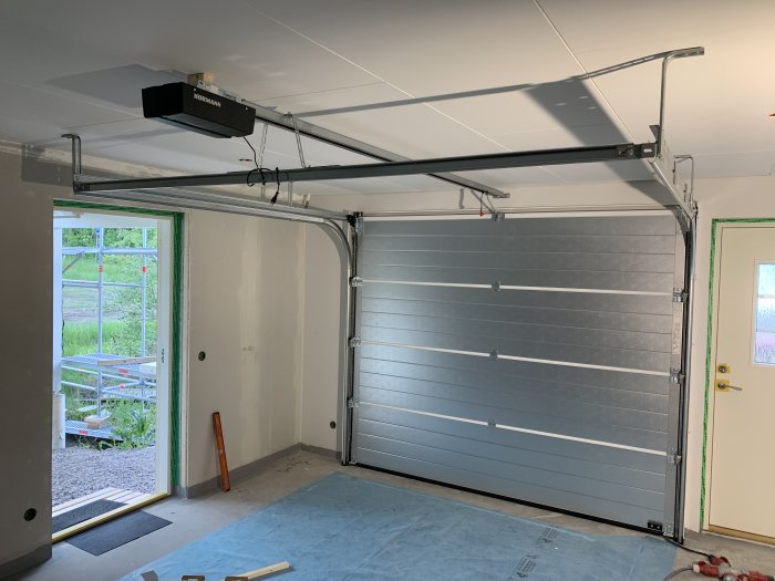 Nyinstallerad garageport i ett garage under byggnation med synliga takskenor och dörröppning.