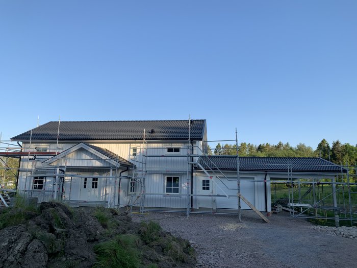 Hus under renovering med byggställningar och en nyligen installerad garageport mot en klarblå himmel.