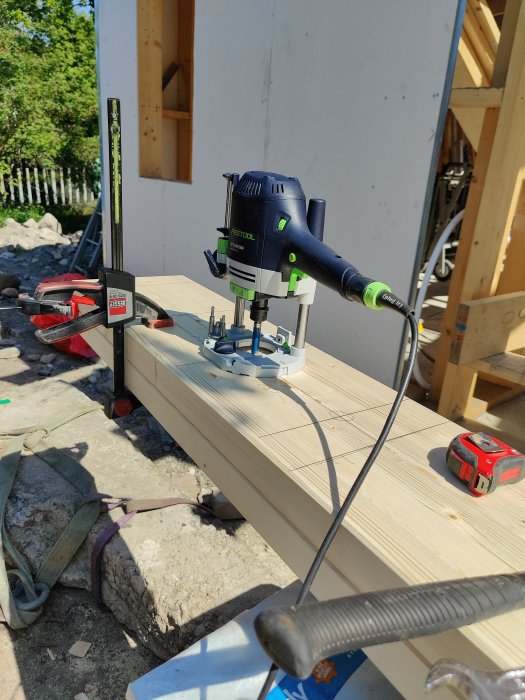 En borr används för att bearbeta en limträbalk i ett pågående byggprojekt, med verktyg och byggmaterial synliga i bakgrunden.