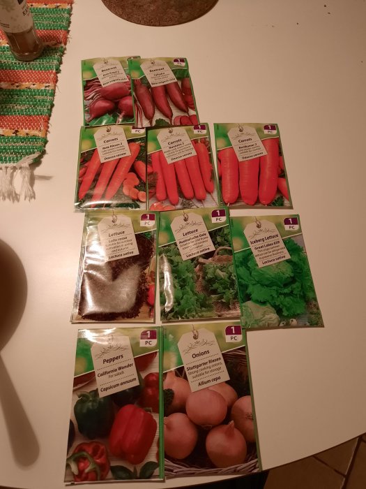 Fröpaket för olika grönsaker, inklusive rödbetor, morötter, sallad och paprika, på bord.