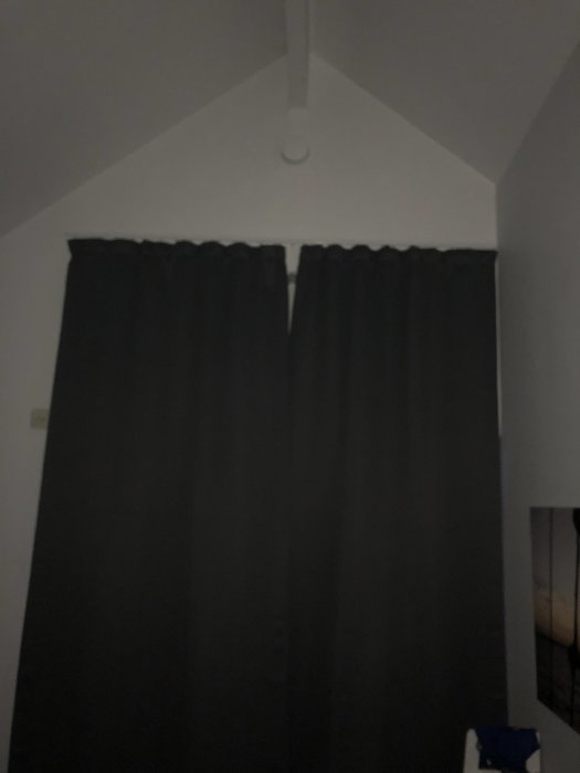 Mörkläggningsgardiner i ett sovrum med spetsig nock och synlig ventil ovanför fönstret.