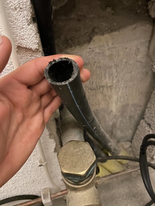 Hand håller ett svart 32mm PEM-rör nära en väggtapp i ett byggprojekt.