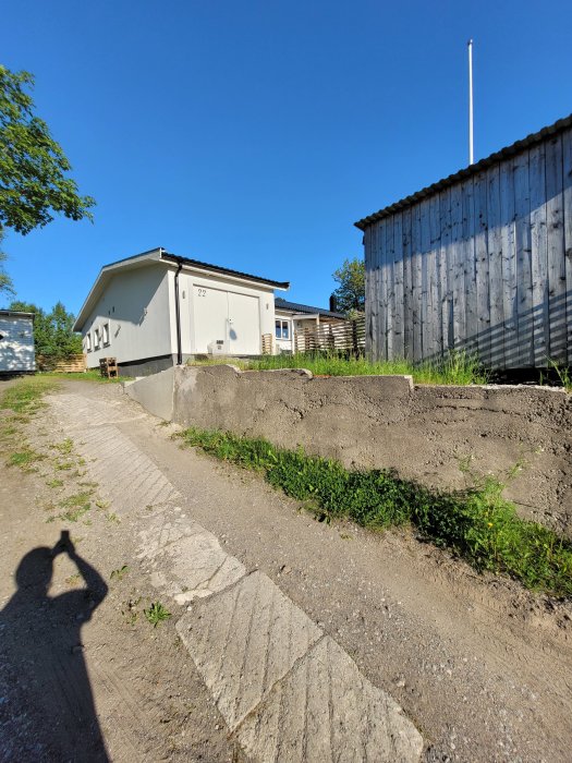 Oasfalterad uppfart med grus och partiell markstensbeläggning som leder till en vit husfasad.