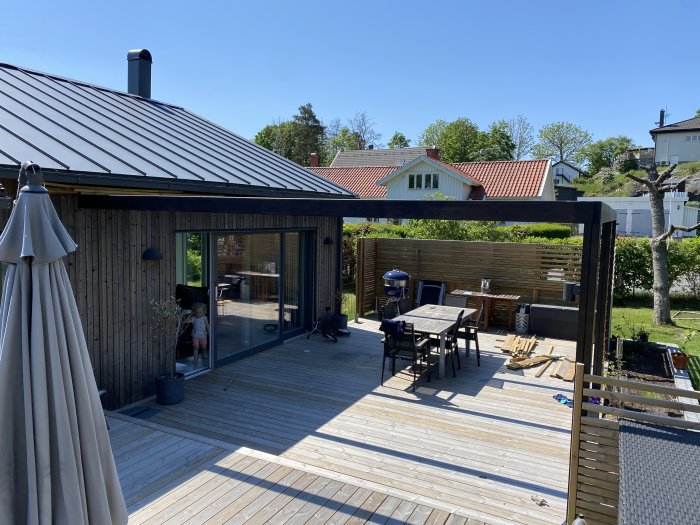 Välunderhållet trädäck med utemöbler och grill vid en modern villa, ingen synbar nedböjning, klart väder.