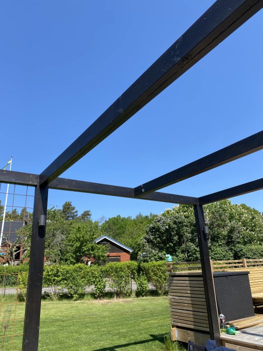 Metallstomme till en pergola under konstruktion i en trädgård en solig dag.