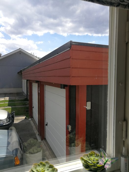 Garage med rödbrun fasad målad med linoljefärg, vit garageport och växt i förgrunden.