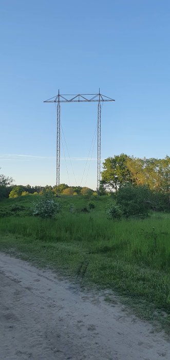 Högspänningsmast utan kablar mot en blå himmel, omgiven av gröna träd och gräs, i en konverteringstest till trådlös överföring.