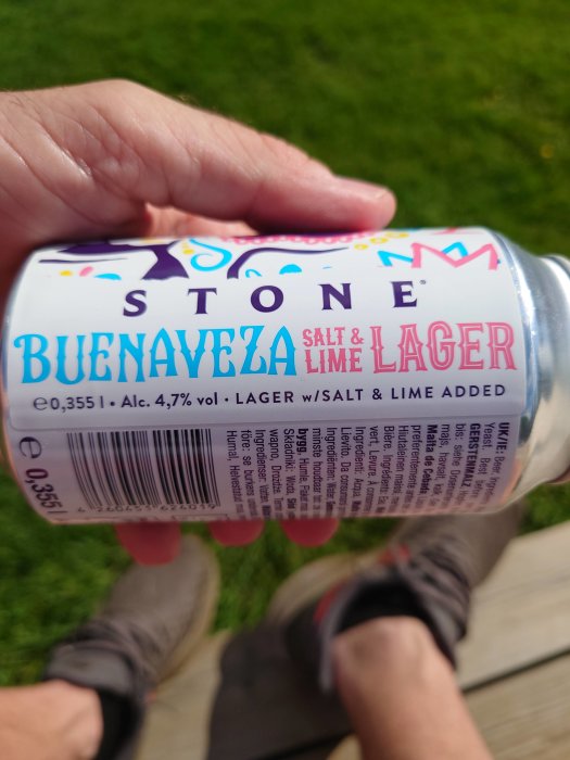 Hand håller en burk Stone Buenaveza Salt & Lime Lager på en gräsmatta.