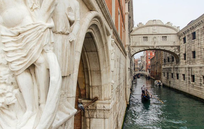 Gondol som glider under den kända Suckarnas bro i Venedig, omgiven av historisk arkitektur.