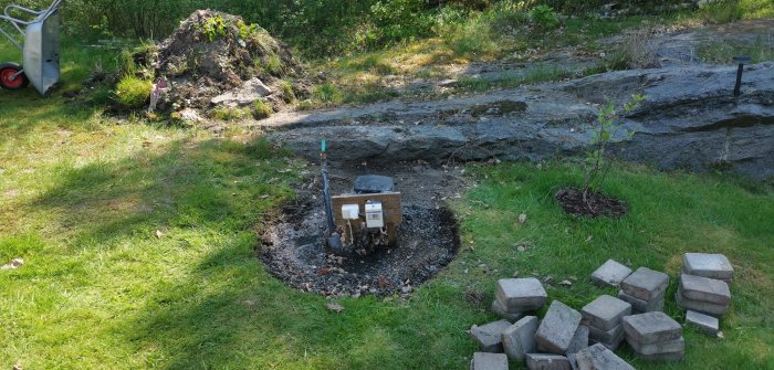 Bild på en trädgårdsbrunn omgiven av gräsmatta och en hög med stenblock nära brunnen.