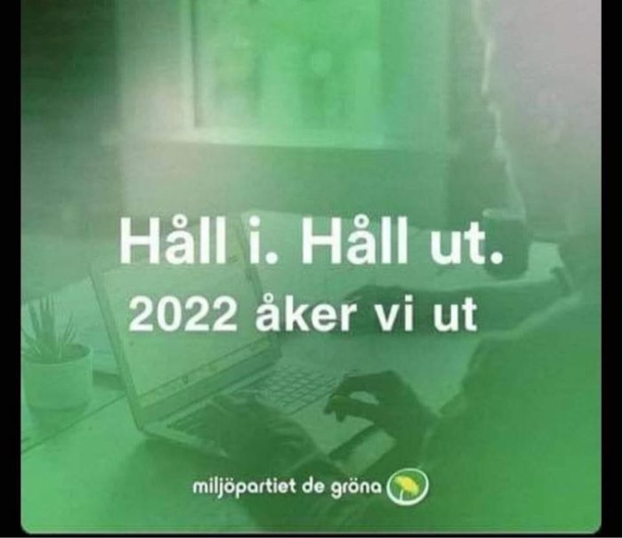 Överskuggad bild av ett arbetsbord med en bärbar dator och en text om att "2022 åker vi ut" från miljöpartiet.