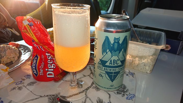 Ett glas med skummande öl bredvid en ölburk från Apex Brewing, och en påse Digestivekex.