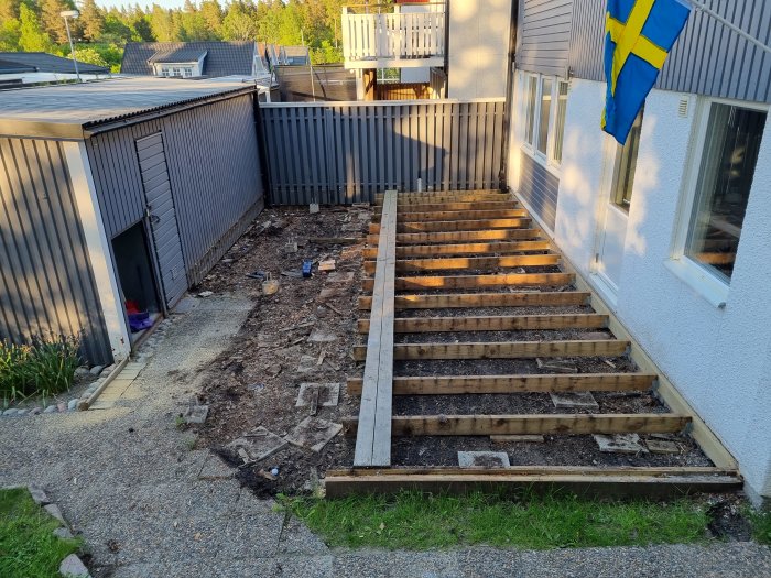 Före-bild av en halvt nedmonterad altan med utsikt över ett hus och förråd, byggavfall syns på marken.