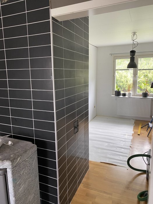 Interiör med öppning för dörr mellan kaklad vägg och vit vägg, golvskydd och golv i förgrunden.
