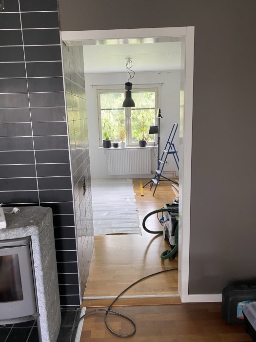 Öppning i vägg för dörrinstallation med utsikt mot ett annat rum och en stege i bakgrunden.