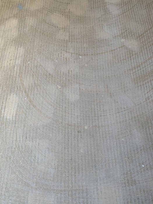 Slipat golv med spår av mattlim och rester, vilket ger en texturerad yta med cirkulära mönster.