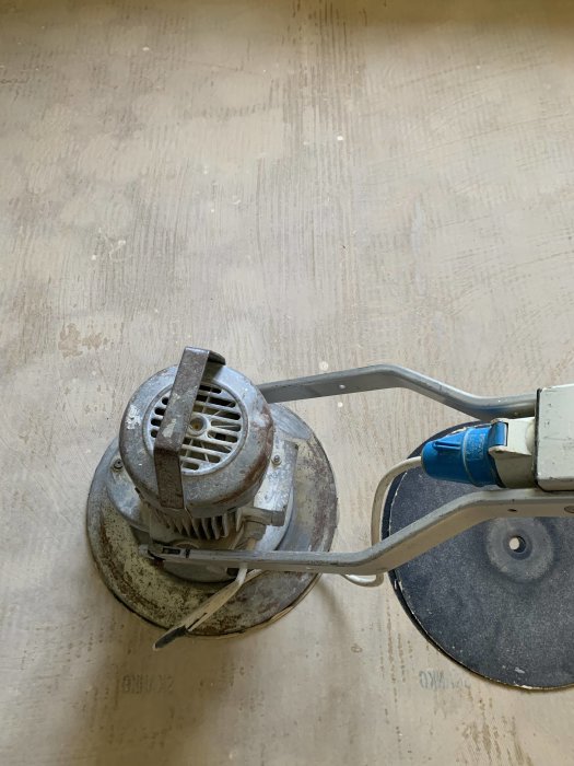 Golvyta som har slipats ren från rester av sisalmatta, med en golvslipmaskin i förgrunden.