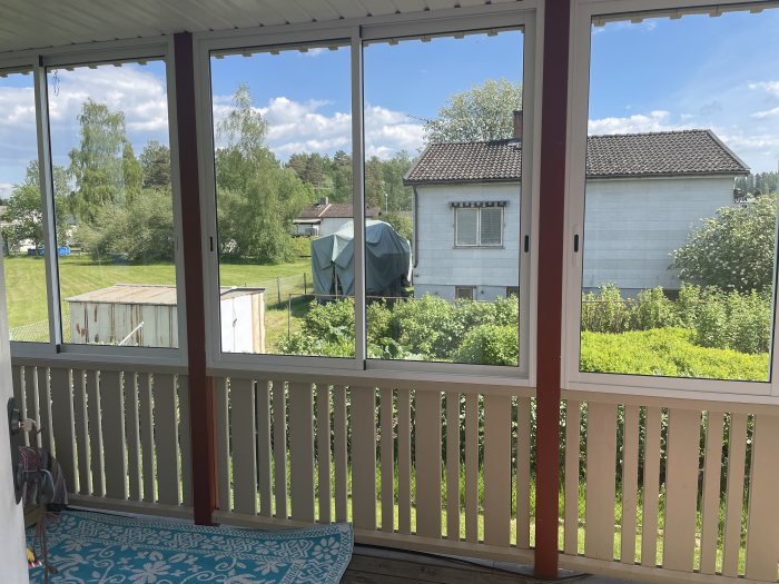 Utsikt från veranda med sommarpartier i aluminiumram, synlig fog mellan regel och ram, över trädgård.