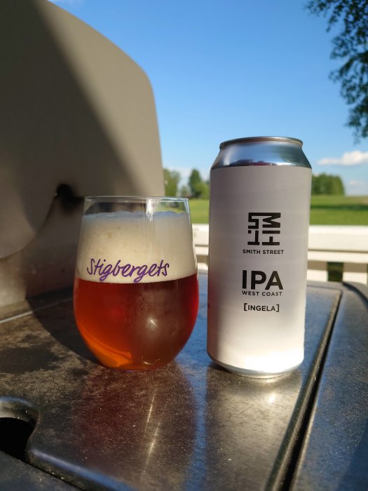 Ölglas märkt Stigbergets och burk med Smith Street IPA på ett bord utomhus.