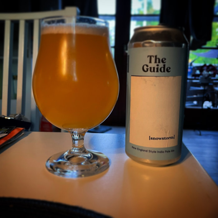 Ölglas fyllt med grumlig öl bredvid en burk märkt "The Guide Snowstorm New England Style India Pale Ale".