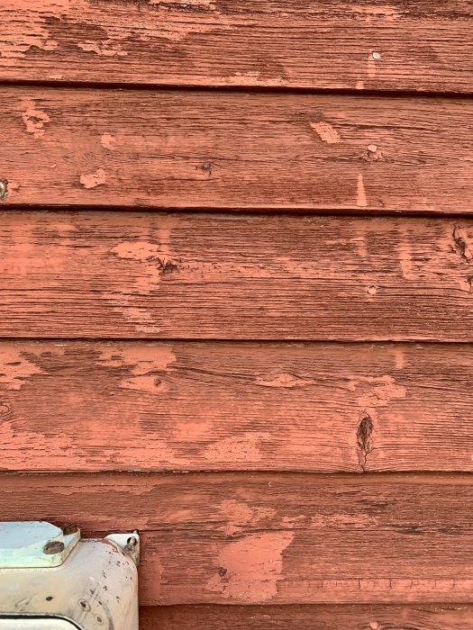 Faluröda träpaneler på en fasad med slitage och avflagningar, behov av underhåll syns.